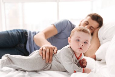 İmge-in küçük çocuk oğlu kamera kapalı evde seyir ederken yatakta uyuyan yakışıklı genç baba baba.