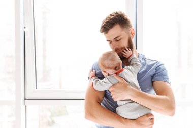 Yakışıklı genç baba baba elinde tutan küçük bebek oğlu kapalı evde görüntüsünü.