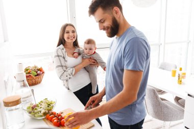 Mutlu genç çift anne mutfakta yemek küçük çocuk bebek oğulları ile sevgi dolu görüntüsünü.