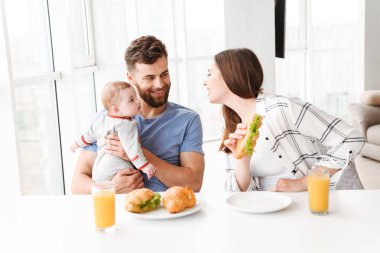 Fotoğraf şirin komik genç çift anne mutfakta yemek küçük bebek oğulları ile sevgi dolu bir kahvaltı var.