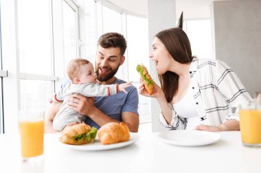 Fotoğraf şirin komik genç çift anne mutfakta yemek küçük bebek oğulları ile sevgi dolu bir kahvaltı var.