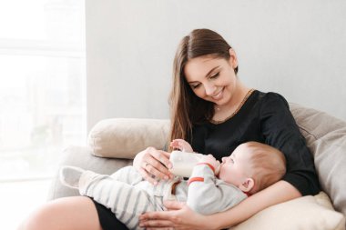 Mutlu genç aile görüntüsü. Anne küçük çocuğunu evde kapalı beslemeleri.