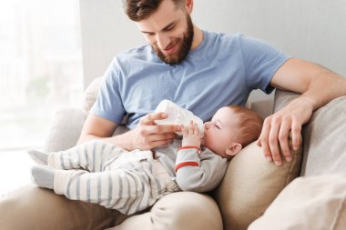 Genç aile görüntüsü. Babası küçük çocuğunu evde kapalı beslemeleri.