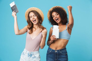 İki farklı renk deri giyen hasır şapkalar ve yaz giyim sevinçli 20'li yaşlarda kızlarla tatil Pasaportlar ve seyahat bilet üzerinde mavi arka plan izole elinde onların tatil