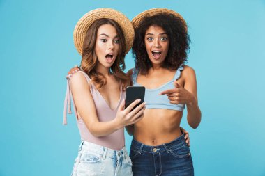 Açık ağız heyecanla ifade ve smartphone ekranında mavi arka plan üzerinde izole selfie çekerken parmakla iki çok ırklı yaz kız tatil fotoğraf
