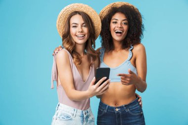 Gülüyor ve smartphone ekranında mavi arka plan üzerinde izole selfie çekerken parmakla iki çok ırklı yaz kız mutlu fotoğraf