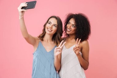 Barış geture izole pembe arka plan üzerinde gösterilen bir selfie alarak elbiseler iki genç ve güzel kız