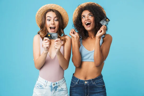 两个快乐的多民族妇女的照片20S 戴着草帽和夏天的衣服尖叫 而持有信用卡隔离在蓝色背景 — 图库照片