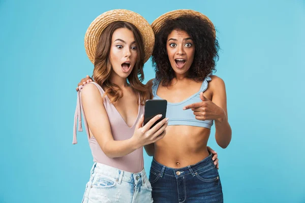 Açık ağız heyecanla ifade ve smartphone ekranında mavi arka plan üzerinde izole selfie çekerken parmakla iki çok ırklı yaz kız tatil fotoğraf