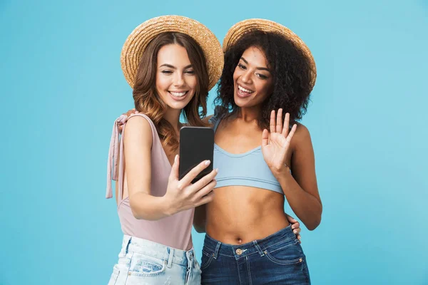 麦わら帽子と笑顔と青い背景に分離された携帯電話で Selfie をしながらカメラに手を振って 夏服を着て つの民族の女の子の休暇の写真 — ストック写真