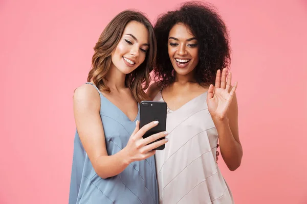 ドレス ピンク背景に分離されたビデオ チャットをしながら携帯電話を保持している つの陽気な若い女の子 — ストック写真