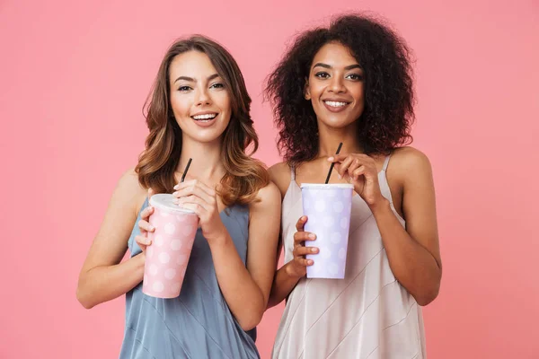 开朗年轻的两个妇女的形象站在粉红色背景饮酒鸡尾酒 — 图库照片