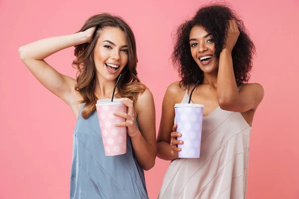 开朗年轻的两个妇女的形象站在粉红色背景饮酒鸡尾酒 — 图库照片