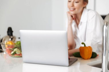 Dizüstü bilgisayar yemek mutfak kapalı evde duran genç güzel kadın kırpılmış görüntü kullanma.