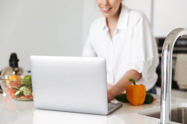 Dizüstü bilgisayar yemek mutfak kapalı evde duran genç güzel kadın kırpılmış görüntü kullanma.