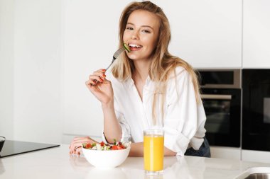 Salata bir kase yemek ve mutfak üzerinde duran portakal suyu içme memnun genç kadın