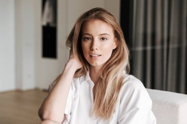 Evde bir kanepede oturan beyaz gömlek giymiş güzel genç kadın