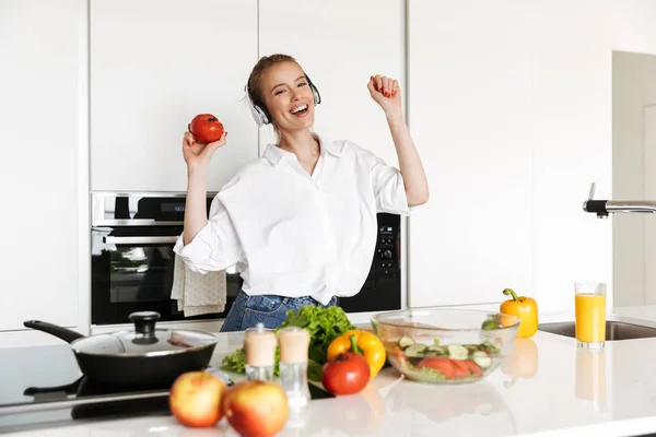 Jovem Alegre Ouvindo Música Com Fones Ouvido Enquanto Cozinha Salada — Fotografia de Stock