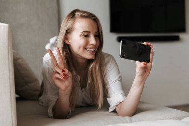 Cep telefonu yapmak selfie tarafından görüntü kapalı evde mutlu sevimli genç kadın yalanların konuşuyor.