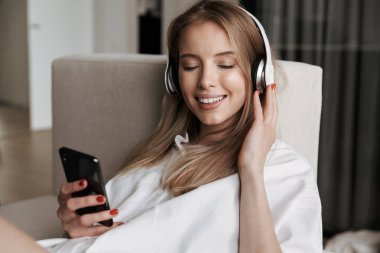 Gözleri kapalı evde bir kanepede döşenmesi sırasında cep telefonuyla Kulaklığımda mutlu genç kadın