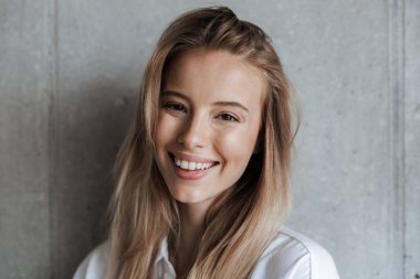 Sevimli güzel genç kadın kapalı kamera seyir gri duvarın üzerinden görüntü.