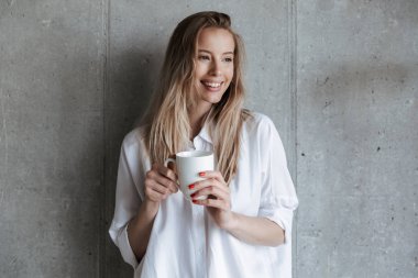 Resmi gri duvar içme üzerinde kapalı şirin mutlu genç kadın kahve holding Kupası.