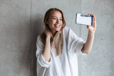 Gri duvar arka plan üzerinde duran bir selfie alarak bir genç ve güzel kız portresi