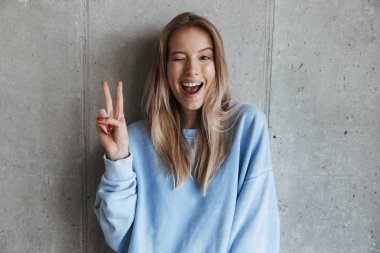 Genç neşeli mutlu güzel kadın kamera gösteren barış hareketi seyir gri duvar arka plan üzerinde duran resim.
