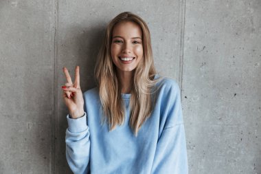 Genç neşeli mutlu güzel kadın kamera gösteren barış hareketi seyir gri duvar arka plan üzerinde duran resim.