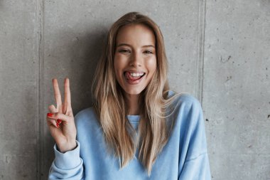 Genç neşeli mutlu güzel kadın kamera gösteren barış hareketi seyir gri duvar arka plan üzerinde duran resim.