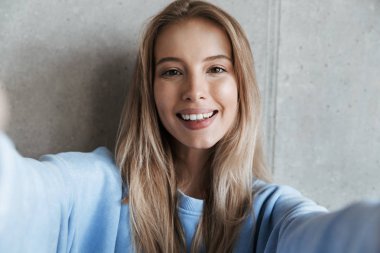 Genç neşeli mutlu güzel kadın kamera tarafından gri duvar arka plan yapmak selfie üzerinde duran resim.