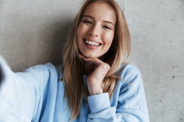 Genç neşeli mutlu güzel kadın kamera tarafından gri duvar arka plan yapmak selfie üzerinde duran resim.