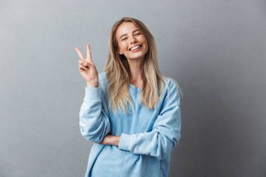 Mavi kazak barış hareketi izole gri arka plan üzerinde gösterilen neşeli bir genç kız portresi