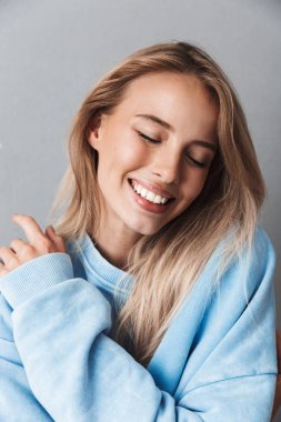Gri arka plan üzerinde izole gülümseyen genç bir kızın gözleri kapalı ile mavi sweatshirt içinde yakın çekim