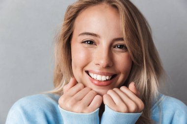 Mavi kazağı gri arka plan üzerinde izole kamera bakarak neşeli bir genç kızın yakın çekim