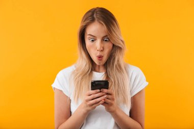 Cep telefonu sarı arka plan izole bakarak şok genç sarışın kız portresi