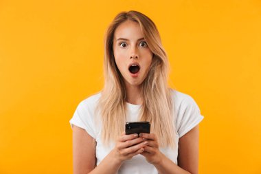 Cep telefonu sarı arka plan izole tutan şok genç sarışın kız portresi