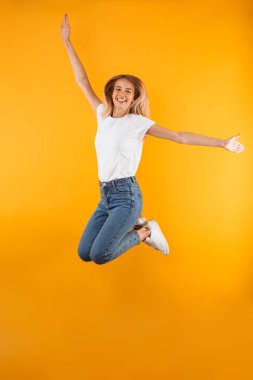 Neşeli bir genç sarışın kız atlama izole sarı arka plan üzerinde iken başarı kutluyor tam uzunlukta portresi