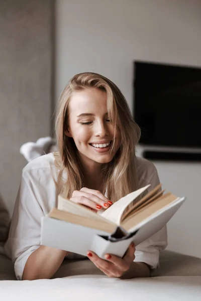 Счастливая Молодая Женщина Читает Открытую Книгу Обложке Бланка Отдыхая Дома — стоковое фото