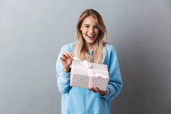 笑顔する灰色の背景上分離した金髪少女アンラッピング プレゼントのボックスの肖像画 — ストック写真