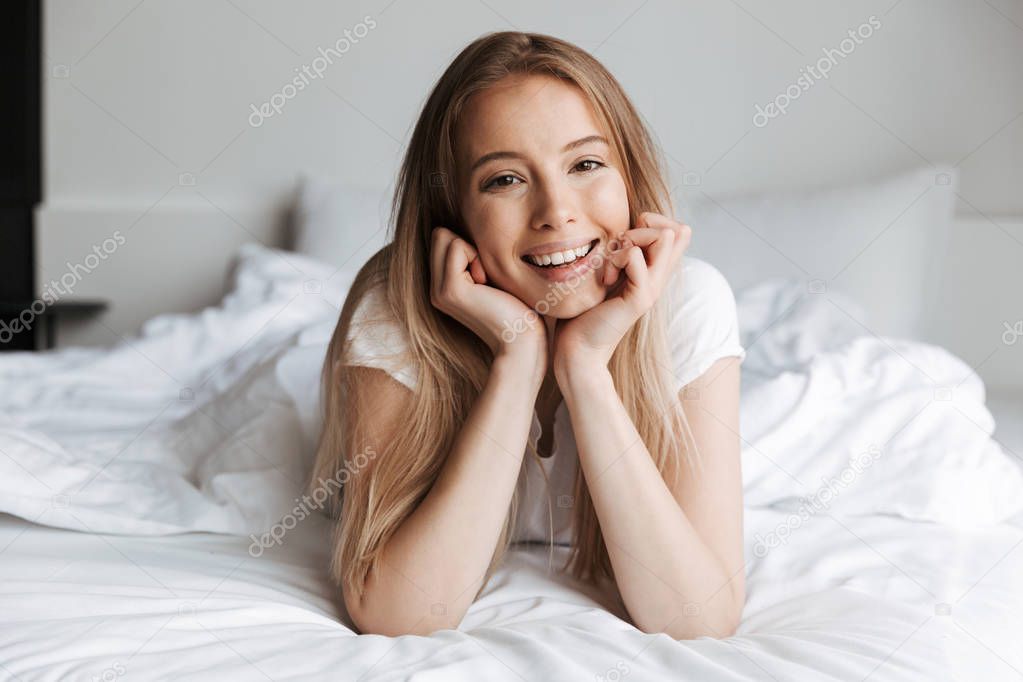 Photo of happy young woman indoors at home looking camera lies in bed.
