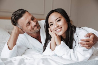 Gülümseyen genç çift yatakta yatarken ve sarılma bornoz giymiş