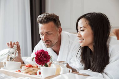 Çekici genç çift yatakta yatarken romantik kahvaltı bornoz giymiş