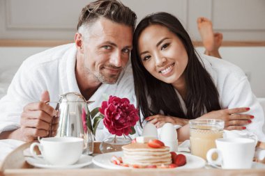 Yatakta yatarken romantik kahvaltı bornoz giymiş güzel genç çift