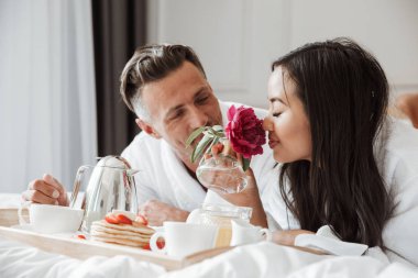 Mutlu genç çift yatakta yatarken romantik kahvaltı bornoz giymiş