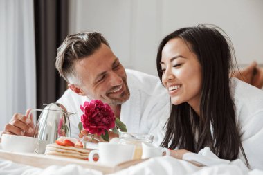 Yatakta yatarken romantik kahvaltı bornoz giymiş genç çift