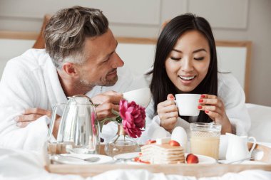Mutlu genç çift yatakta yatarken ve kahve içme sırasında romantik kahvaltı bornoz giymiş