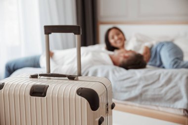 Çift erkek ve kadın jeans birlikte dinlenme ve ön planda odaklı Bagaj ile otel odasında yatakta yatarken giyim gülümseyen bir fotoğraf. Tatil ya da tatil kavramı