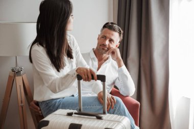 Görüntü güzel çift erkek ve rahat giyim birlikte otel odasında koltuk ve Bagaj elinde tutan birbirine bakarak otururken giyen kadın