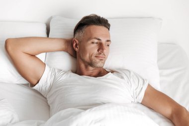 Yatakta rahatlatıcı ve uzağa bakarak gülümseyen adam